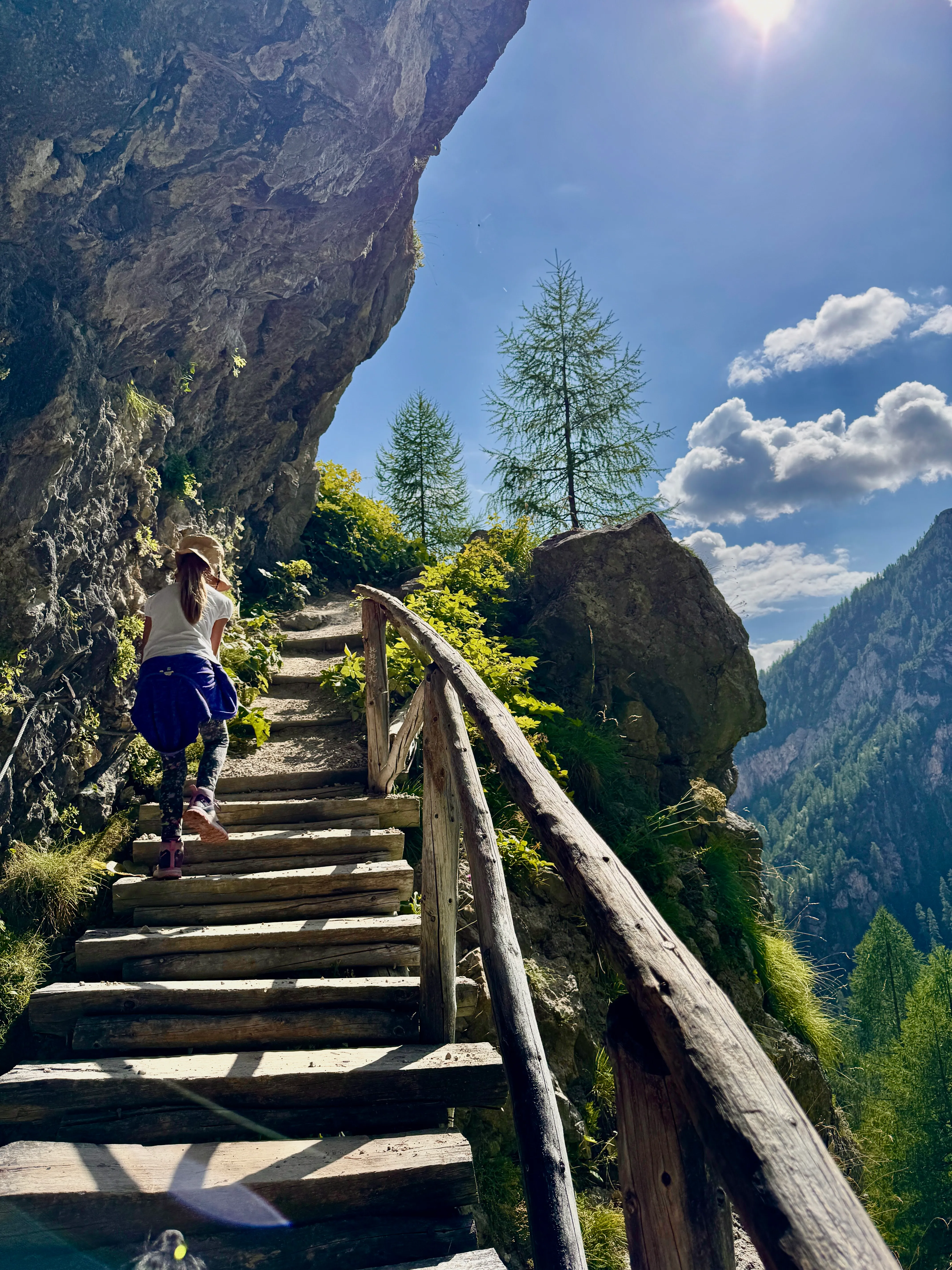 Child climbing wooden steps through a narrow rock passage on the off-road trail to Rifugio Malga Ombretta