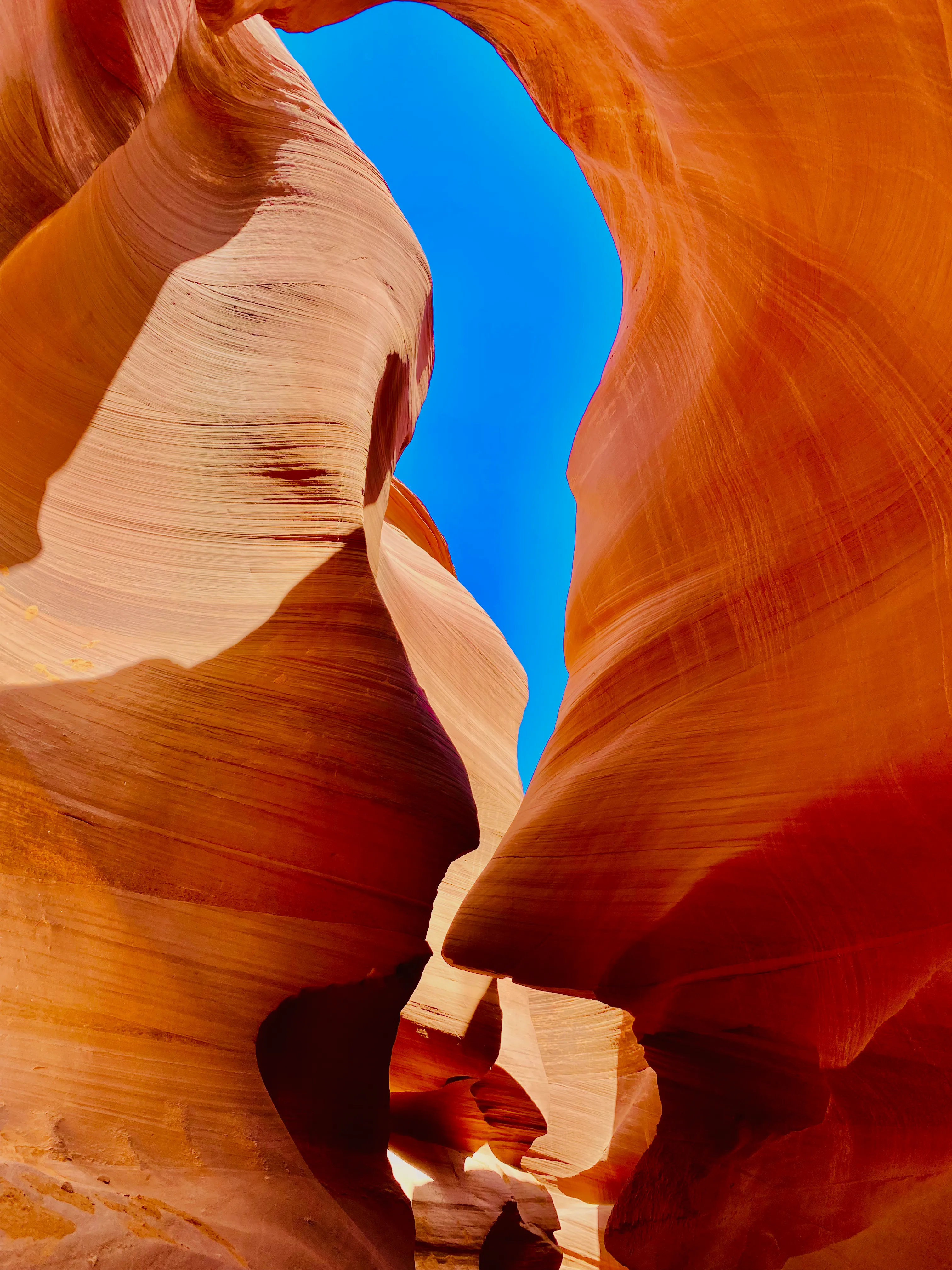 A narrow slot in Antelope Canyon with blue sky visible far above the sandstone walls