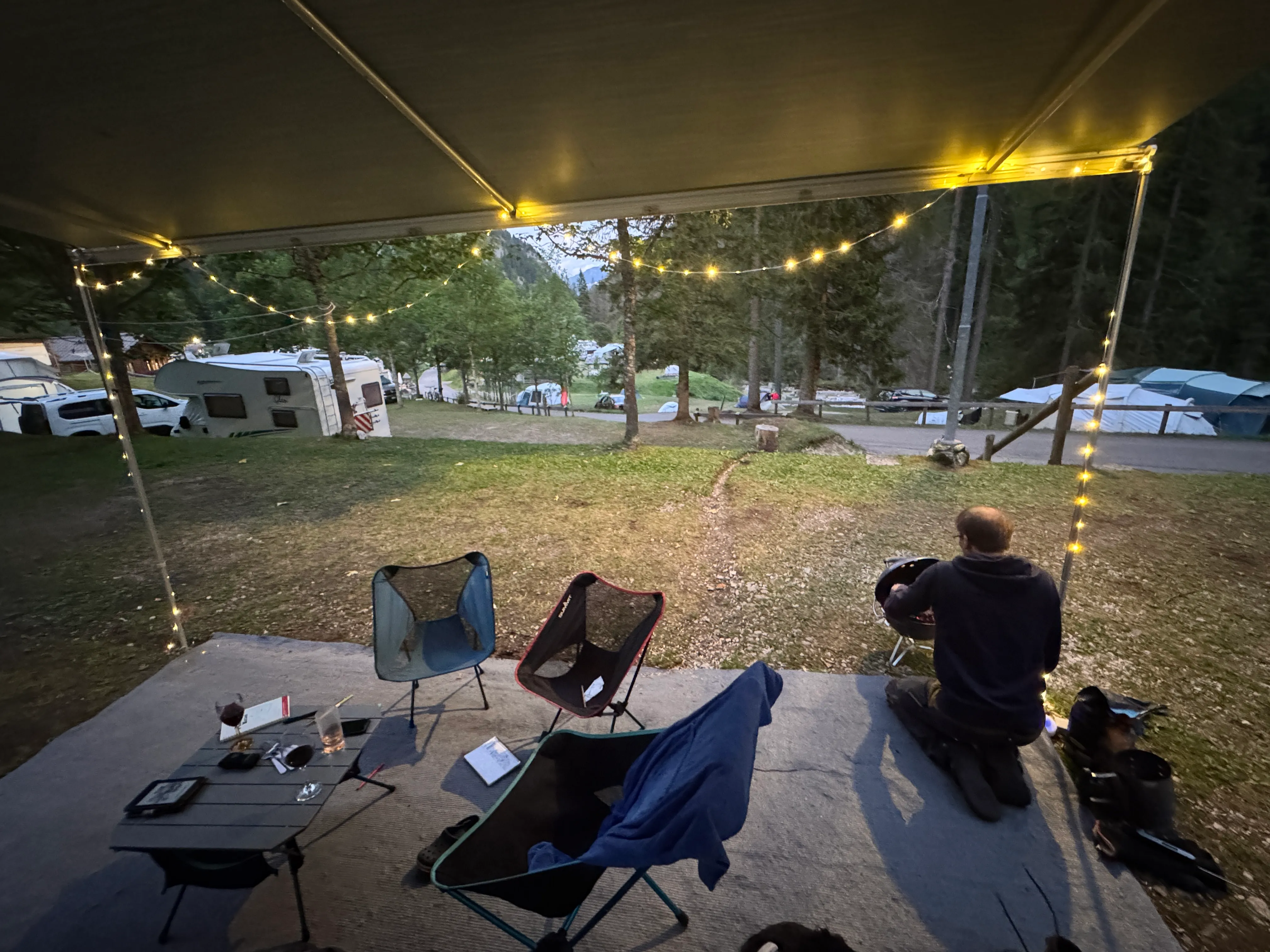 Fairy-lit campsite pitch at dusk with camping chairs, a barbecue and motorhomes at Camping Marmolada