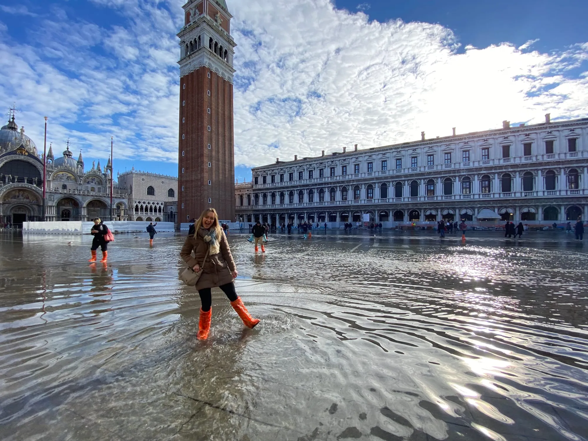 Becky wearing bright orange wellies while wading through a flooded St Mark’s Square in Venice