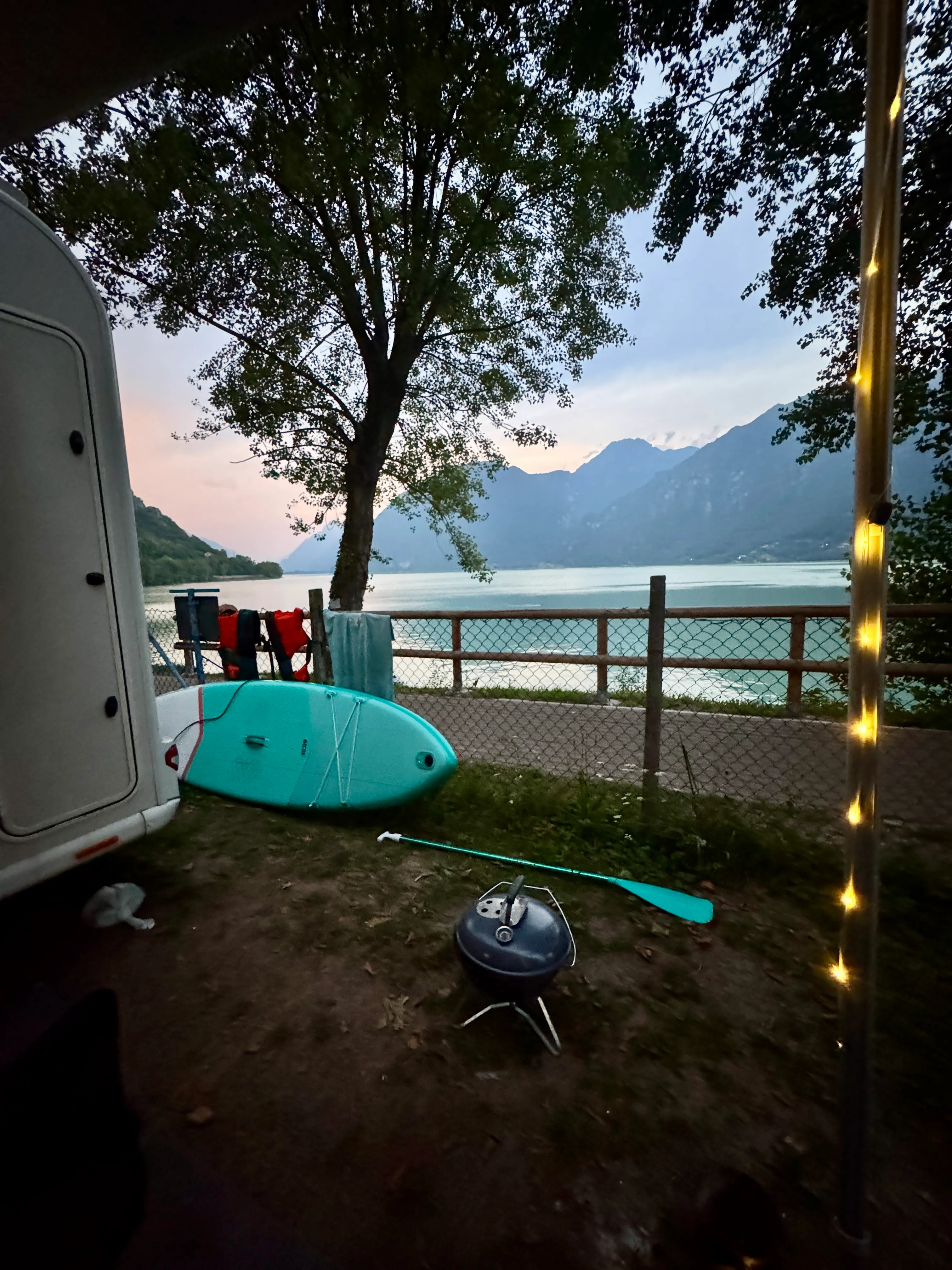 Lakeside campsite pitch at Camping Pilu, Lago d’Idro, with a paddleboard and motorhome by the water at dusk