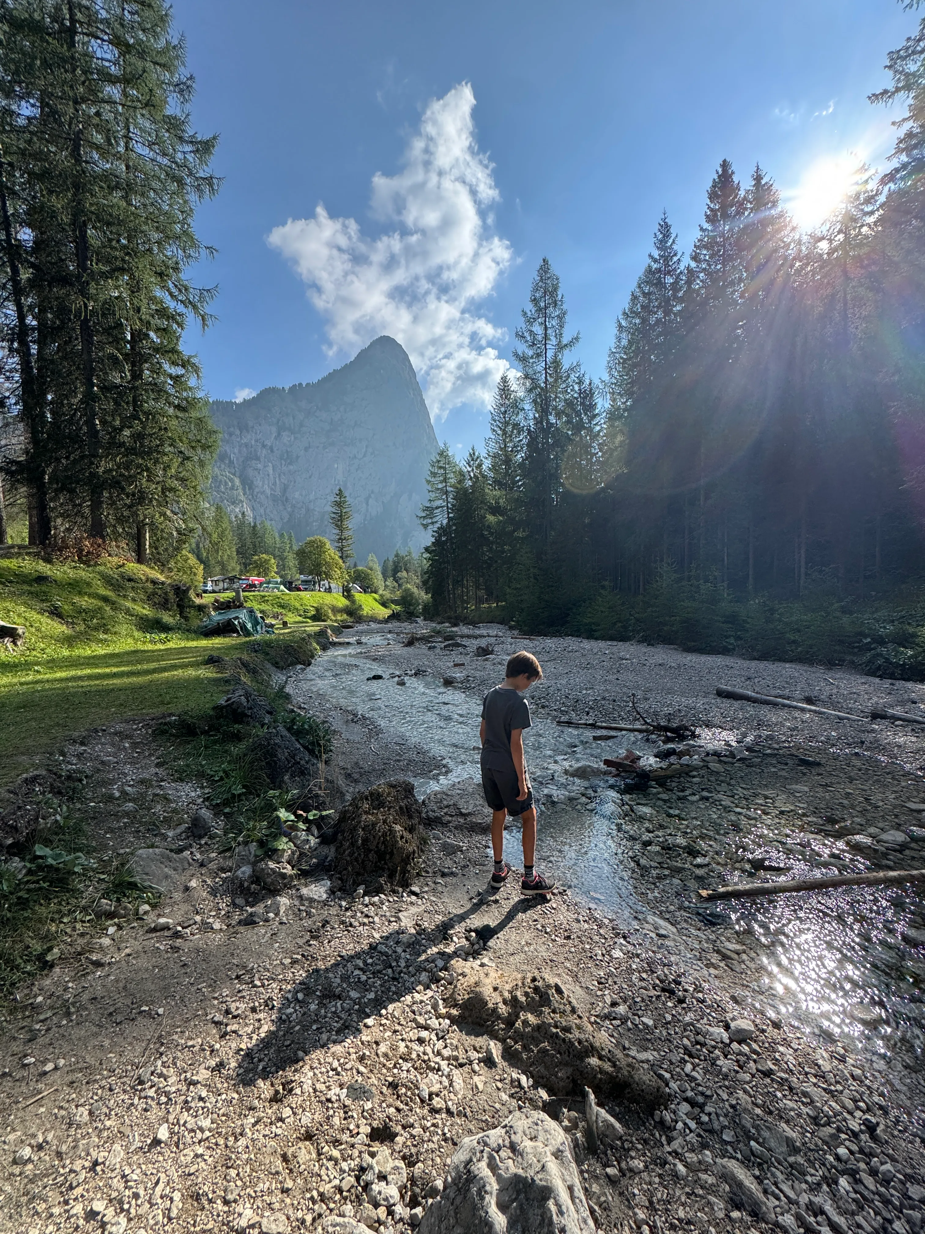 A boy paddling in the shallow river running through Camping Marmolada campsite in Malga Ciapela