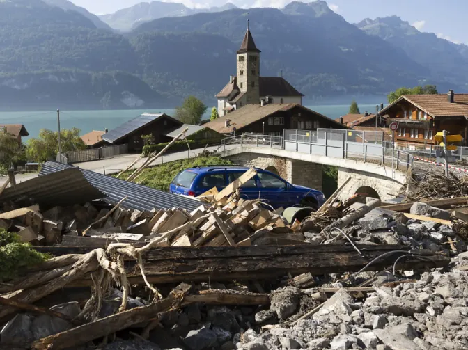 Storm debris of rock, timber and rubble piled up in Brienz village after the August 2024 flood, with the village church behind