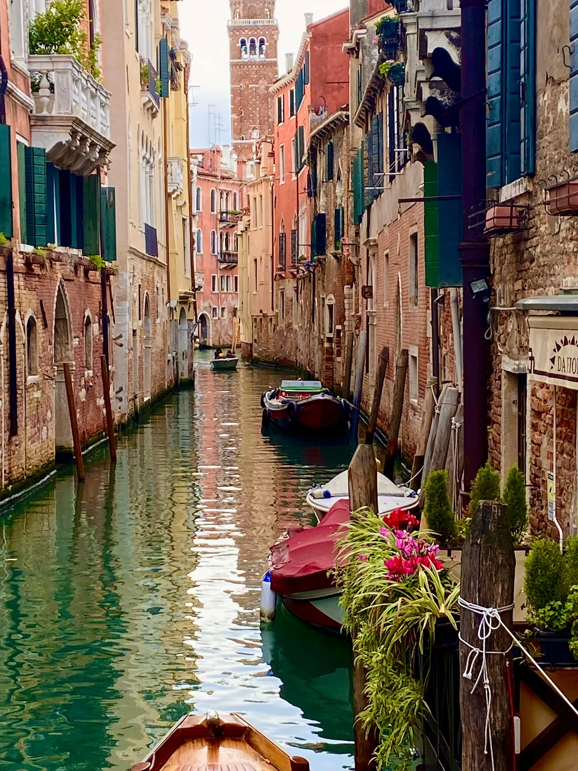 A quiet Venice canal lined with moored boats and pastel-coloured buildings, a bell tower rising behind